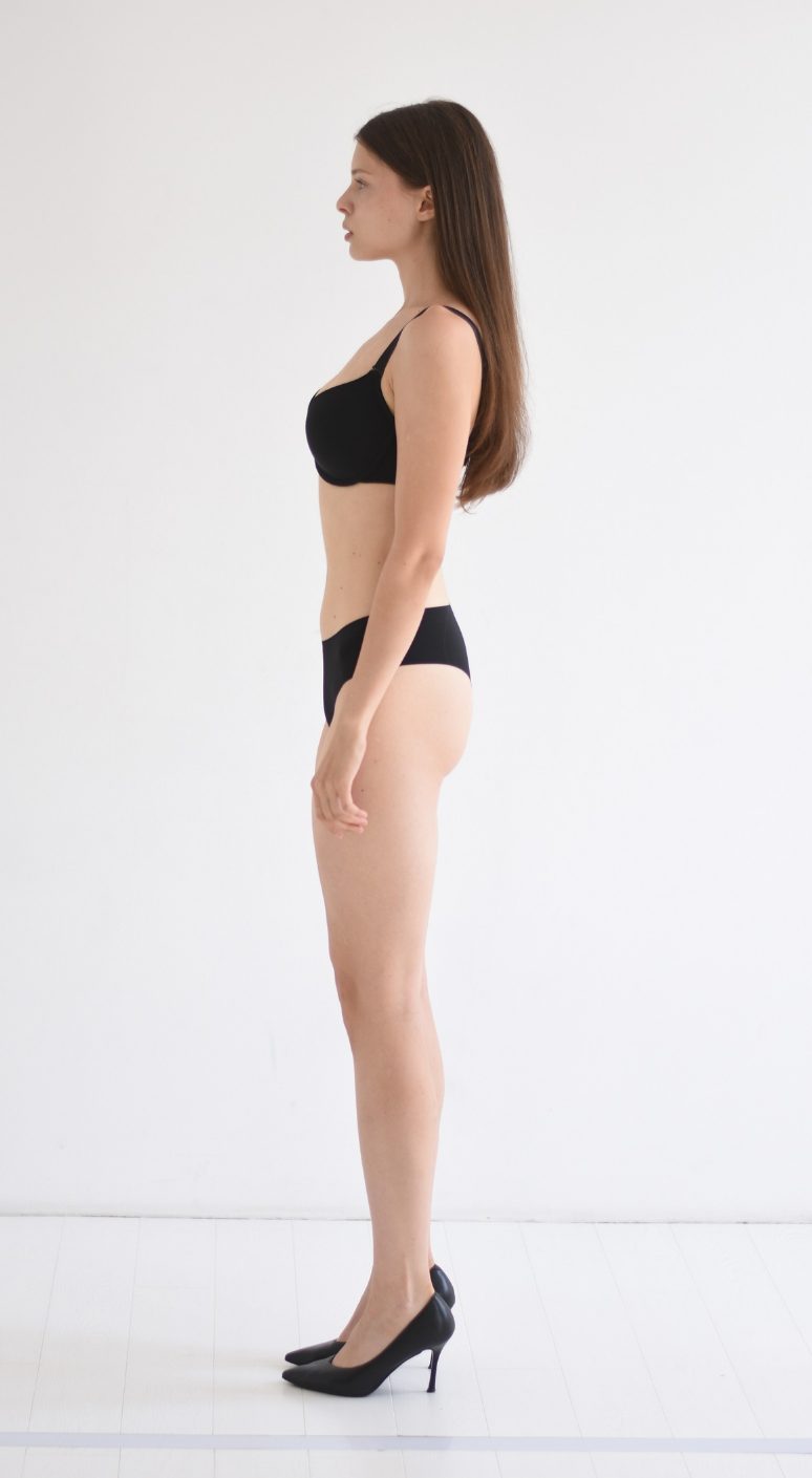Full-body digital of a female model, side view, head to toe against a plain wall